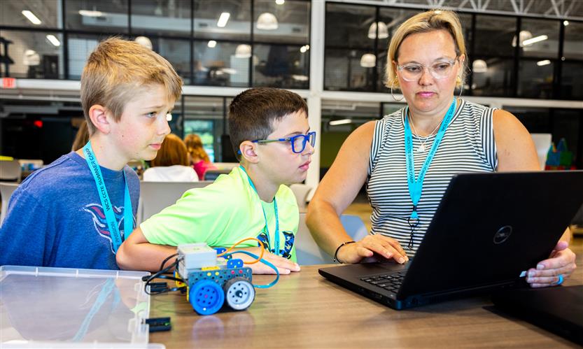 A teacher helps two boys with work on a laptop